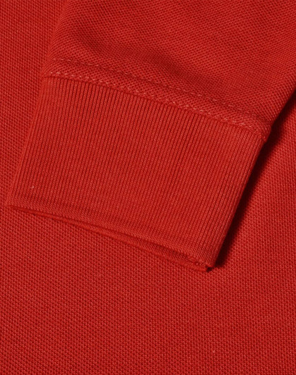 A close-up of a red long sleeve polo shirt, featuring a ribbed cuff and textured fabric.