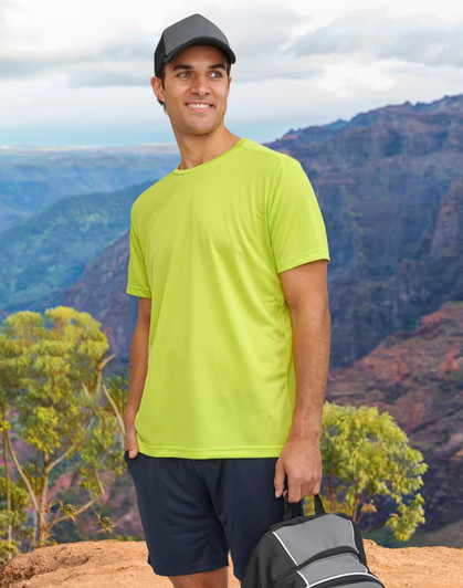 A man wearing a bright yellow short-sleeve performance T-shirt stands against a mountainous backdrop, holding a bag.