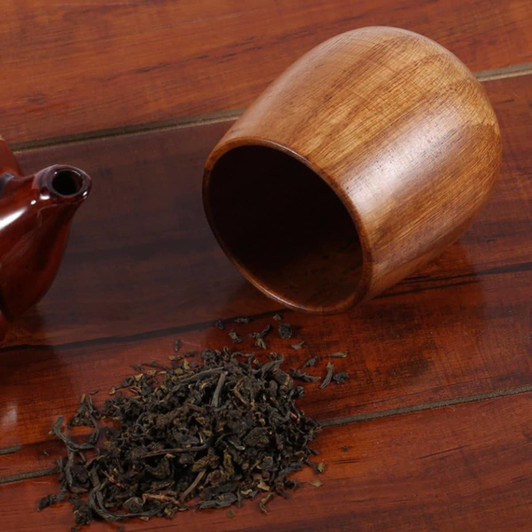A small wooden coffee cup in a rich brown hue, beside loose tea leaves and a teapot.