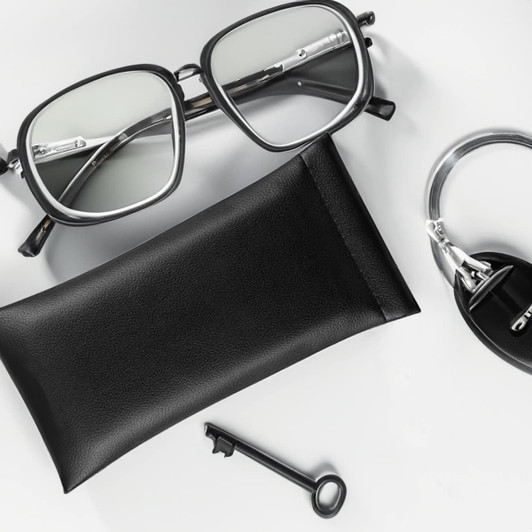 A black PU pouch beside silver glasses, a key, and a keyring. The pouch has a simple design and a logo.