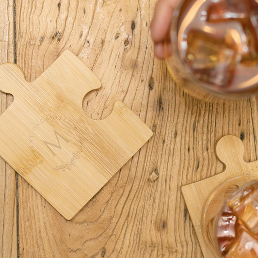 A bamboo coaster set featuring puzzle piece designs, showcasing a light wooden finish and a drink beside it.