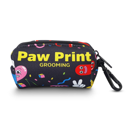 A small black pouch with colourful cartoon prints, featuring a clip and the words "Paw Print Grooming."