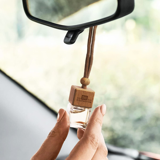 A refillable car air freshener with a wooden cap and clear glass container, hanging from a car mirror.