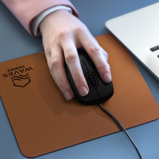 A leatherette mouse mat in brown with a black mouse resting on it, beside a laptop.
