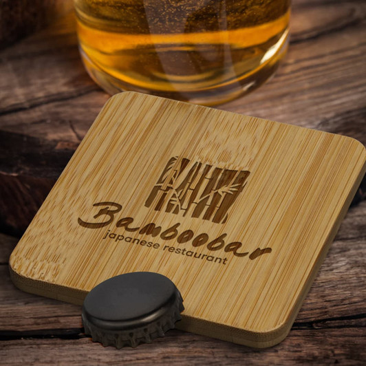 A drink bottle opener coaster made of bamboo, featuring a logo, placed on a wooden surface near a beverage.