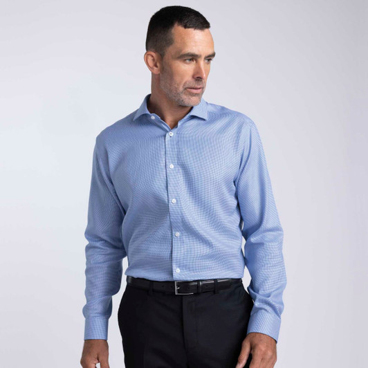 A men's button-up shirt in light blue fabric, featuring a collar and buttons, worn with black trousers.