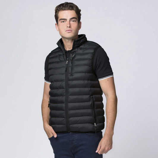 A black padded vest with a high collar, featuring a zip-up front and a logo. An individual poses wearing it.