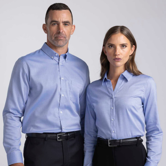 A women's button-up shirt in light blue with a collar and a logo. Paired with formal black trousers.