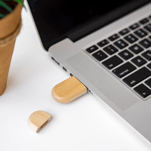 A bamboo USB flash drive is plugged into a laptop, with a cap resting beside it on a white surface.