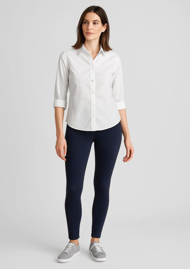 A woman stands wearing a white shirt and navy high-rise pull-on leggings, with grey shoes and a neutral background.