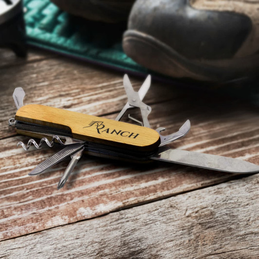 A wooden pocket knife with multiple tools, featuring a corkscrew and blade, set on a wooden surface.