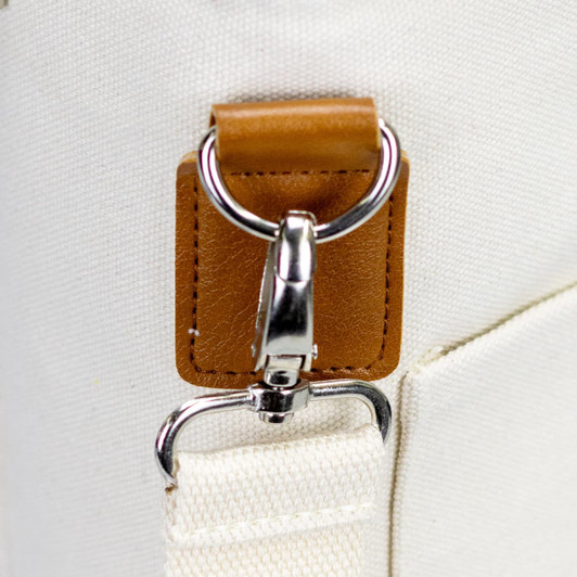 A close-up of a cream-coloured bag featuring a silver clip and a brown leather accent. The bag has a simple design.