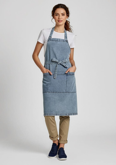 A denim apron in blue, worn by a model over a white t-shirt, featuring pockets and a tied waist.