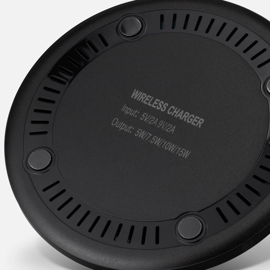 A wireless charger in black with circular design and ventilation holes, featuring a branding logo on the underside.
