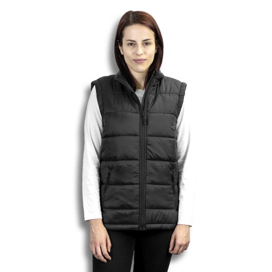 A woman wearing a black puffer vest with a high collar and zip front, styled over a long-sleeve white top.