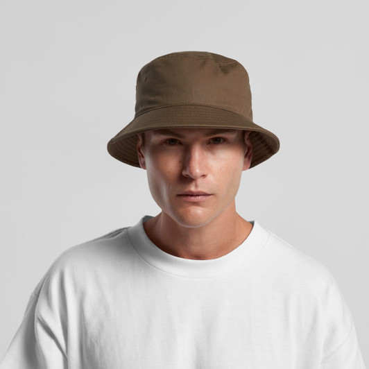 A brown bucket hat with a wide brim, worn by a model in a white t-shirt. The hat features a logo.