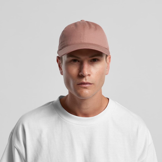 A cap in a soft pink shade, featuring a curved brim and an adjustable back, worn by a model in a white top.