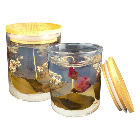 A floral candle in a glass jar with a wooden lid, featuring preserved flowers and leaves in clear wax.