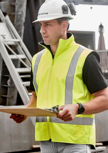 A man wearing a bright yellow waterproof reversible vest with reflective stripes, holding a clipboard.