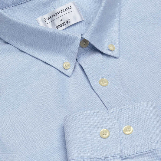 A light blue button-up shirt with a collar, featuring a branding label and light-coloured buttons.