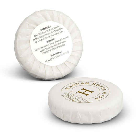 A round, white travel soap with a decorative logo and packaging, featuring a floral design.