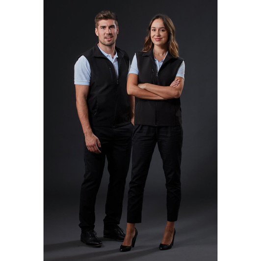 A black softshell vest is worn by a man and woman standing together against a dark background. The vest features a logo.