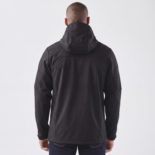 A black softshell jacket with a hood, featuring a logo, shown from the back on a model.