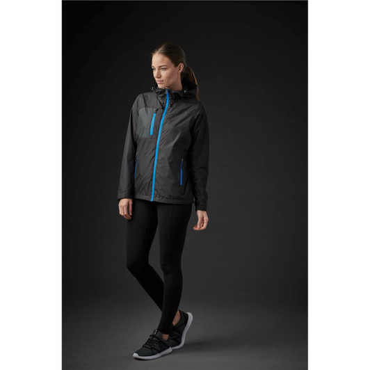 A woman wearing a black rain jacket with blue zippers, paired with black leggings and sporty shoes, against a dark background.