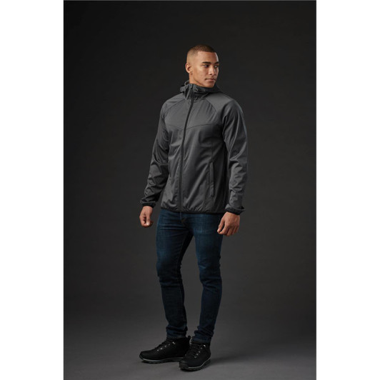 A man wearing a grey softshell jacket stands against a dark background, showcasing a sleek design and fitted style.