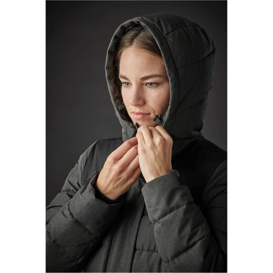 A woman wearing a dark green parka with a hood, adjusting the front zipper. The jacket features a puffy design.