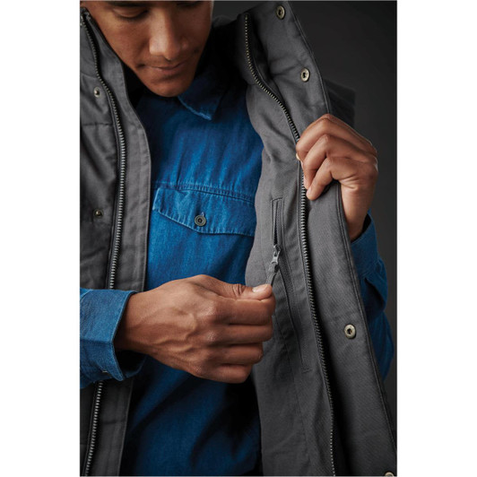 A man wearing a grey thermal vest, showcasing a zip pocket on the inner lining over a blue shirt.