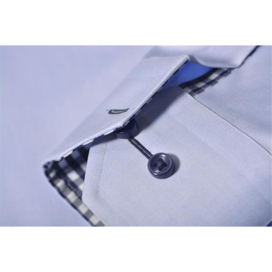 A close-up of a light blue button-up shirt, featuring a checkered inner collar and a dark button. The shirt has a logo.