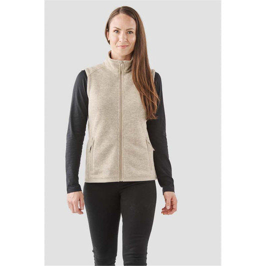 A woman is wearing a beige full zip fleece vest over a black long-sleeve top, featuring side pockets.