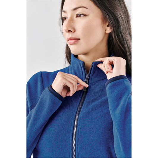 A woman models a women's jacket in a rich blue hue, featuring a full zip and a high collar. The jacket has a logo present.