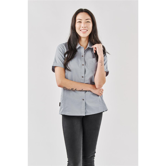 A button-up women's shirt in grey, featuring short sleeves and a neat collar, modelled by a smiling woman.