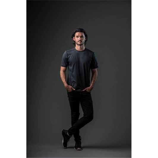 A model wearing a short-sleeved dark grey T-shirt and black jeans, standing against a neutral background.