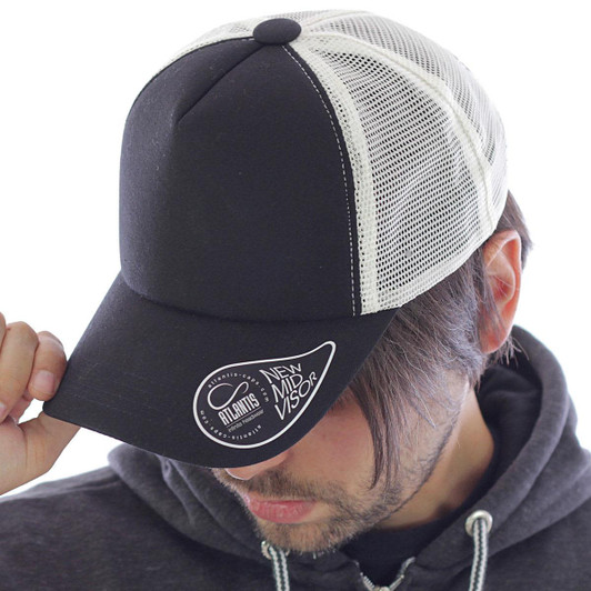 A black and white trucker cap with a mesh back and a logo on the front, worn by a person.