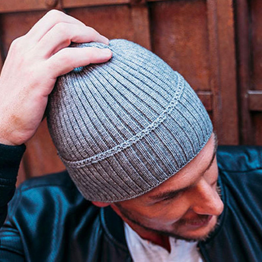 A grey ribbed beanie worn by a person. The beanie has a fitted design and a subtle logo on it.