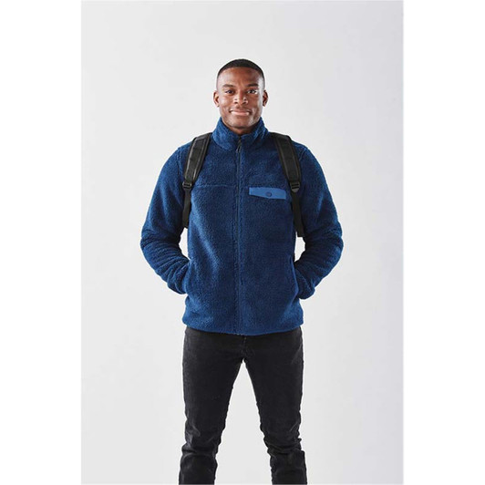 A man wearing a navy blue fleece jacket with a backpack, standing against a plain background.