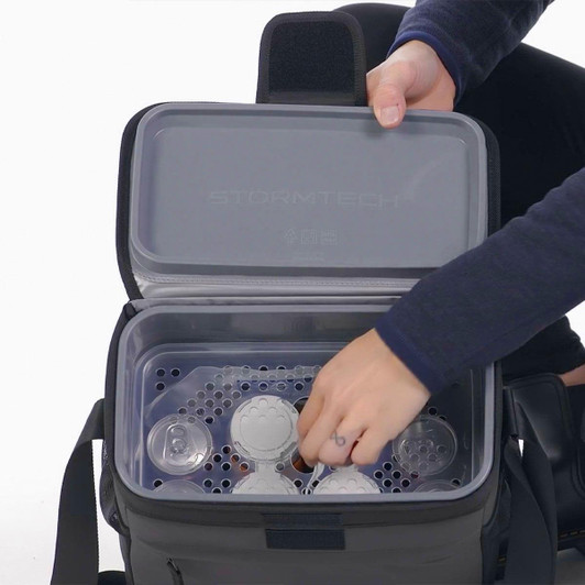 A cooler bag in black, filled with containers and a clear lid, featuring a person reaching inside.
