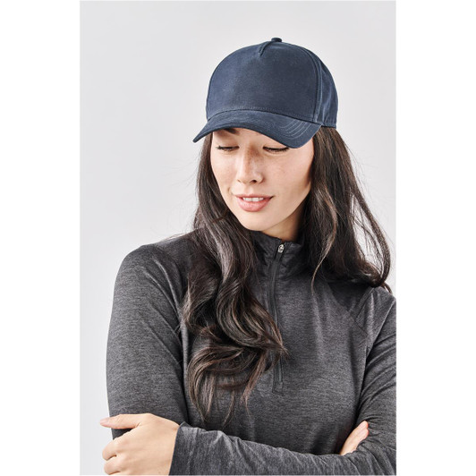 A navy Explorer Cap on a woman with long, dark hair, wearing a grey zip-up top. The cap features a logo.