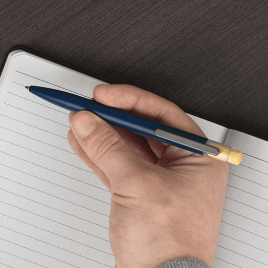 A blue recycled aluminium pen with a bamboo clicker is held above a lined notepad. The pen has a silver clip.