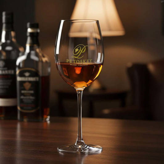 A wine glass with a stem, filled with amber liquid, featuring a logo, set against a softly lit background.