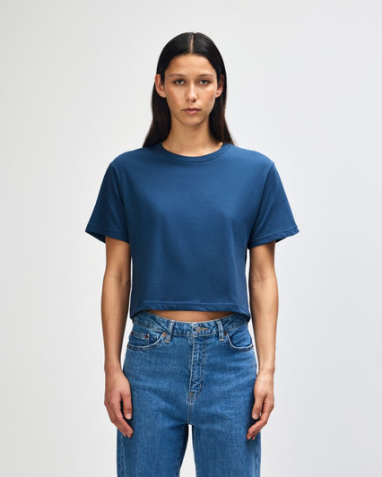 A woman wearing a blue boxy cropped t-shirt paired with high-waisted jeans, standing against a plain background.