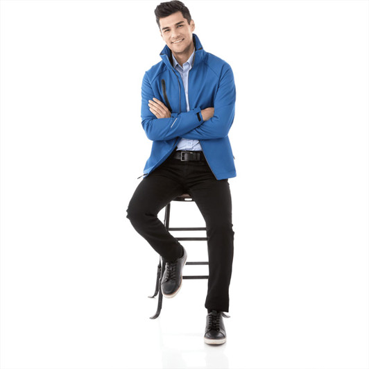 A blue men's softshell jacket with a model seated on a stool, wearing black pants and shoes. The jacket has a logo.