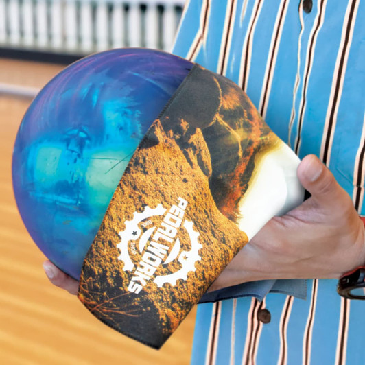 A bowling ball with a blue and purple design, held by a person in a striped shirt. The ball is wrapped with a branded cloth.