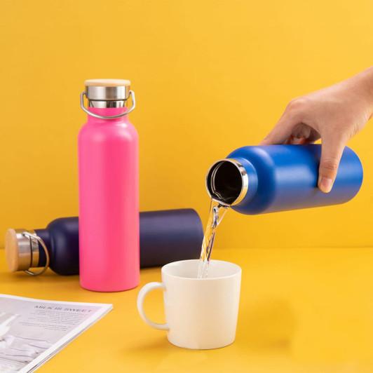 A drink bottle in vibrant pink and blue, with a stainless steel lid, is being poured into a white mug.
