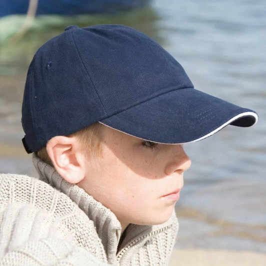 A navy blue cap with a white trim, worn by a child sitting by the water, featuring a logo on the front.