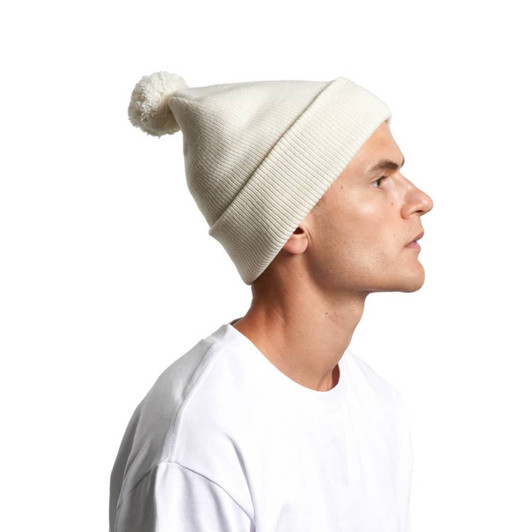 A light cream pom pom beanie worn by a person, featuring a fluffy top and ribbed texture.