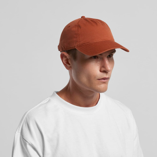 A five panel cap in a burnt orange colour, worn by a model, featuring a logo on the side.